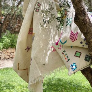 Handwoven Moroccan wool picnic blanket with neon bright accents and bold embroidered patterns, laid out on grass, showing soft fringed edge.